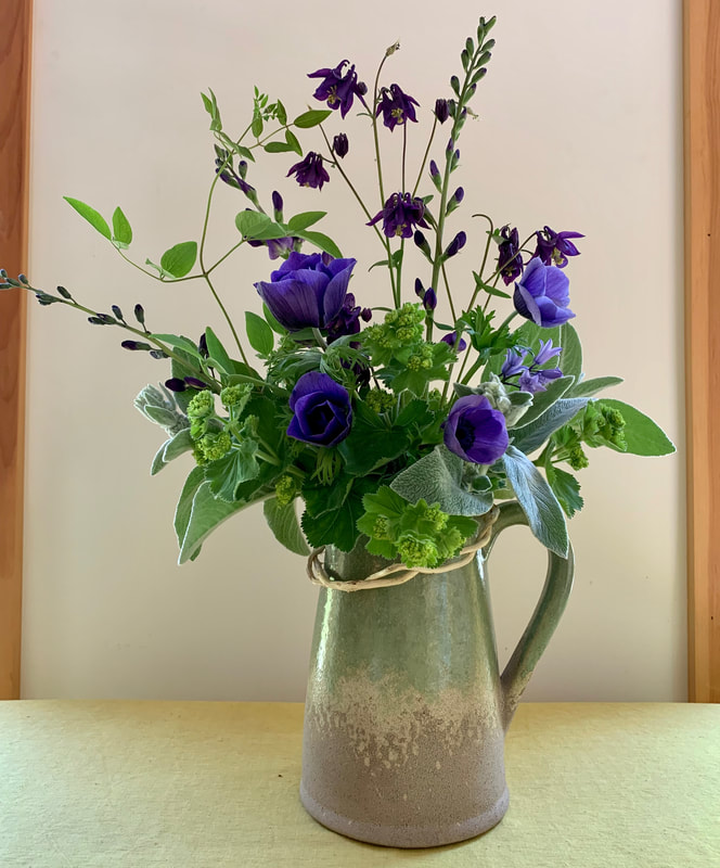 In this arrangement, the gently shifts in colour from the soft mauve of the English Bluebells followed by the false indigo, columbine  and the rich purples of the anemones. The woven American bittersweet vine helps to connect the flowers to the vase. Photo by Foraged Florals.